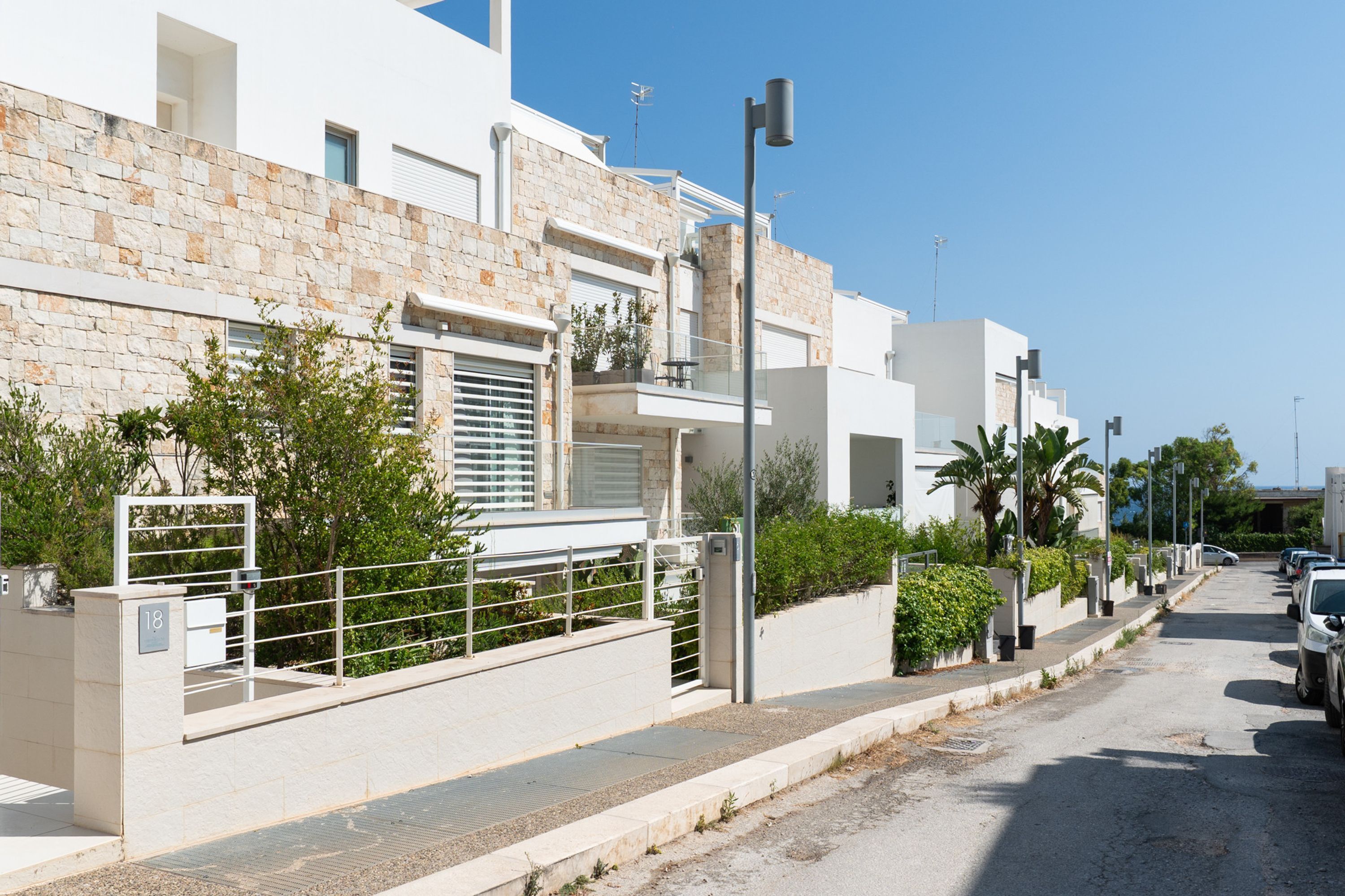 Uma rua residencial moderna com edifícios brancos, um portão e carros estacionados.