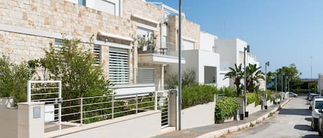 A modern residential street with white buildings, a gated entrance, and parked cars.
