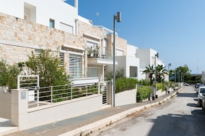 Uma rua residencial moderna com edifícios brancos, um portão e carros estacionados.