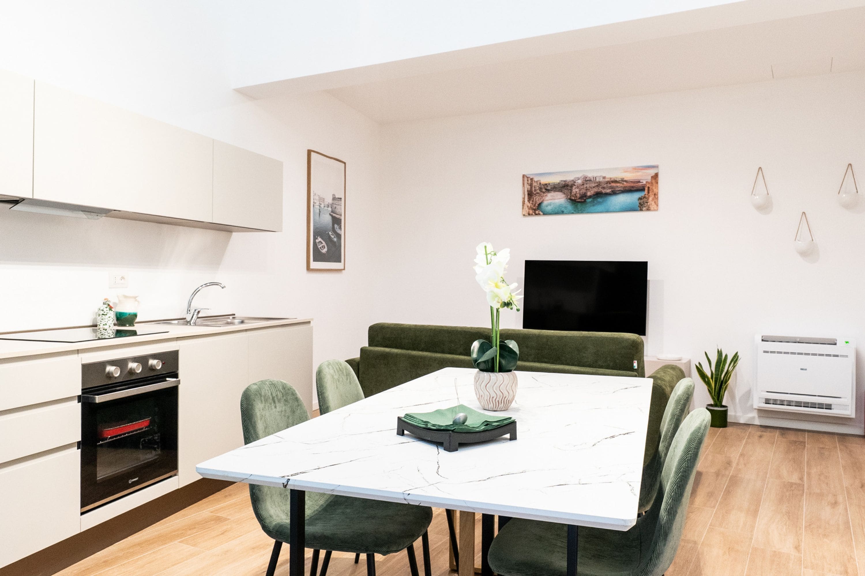 A modern kitchen with white cabinets, a built-in oven, and a dining area with a white table and green upholstered chairs.