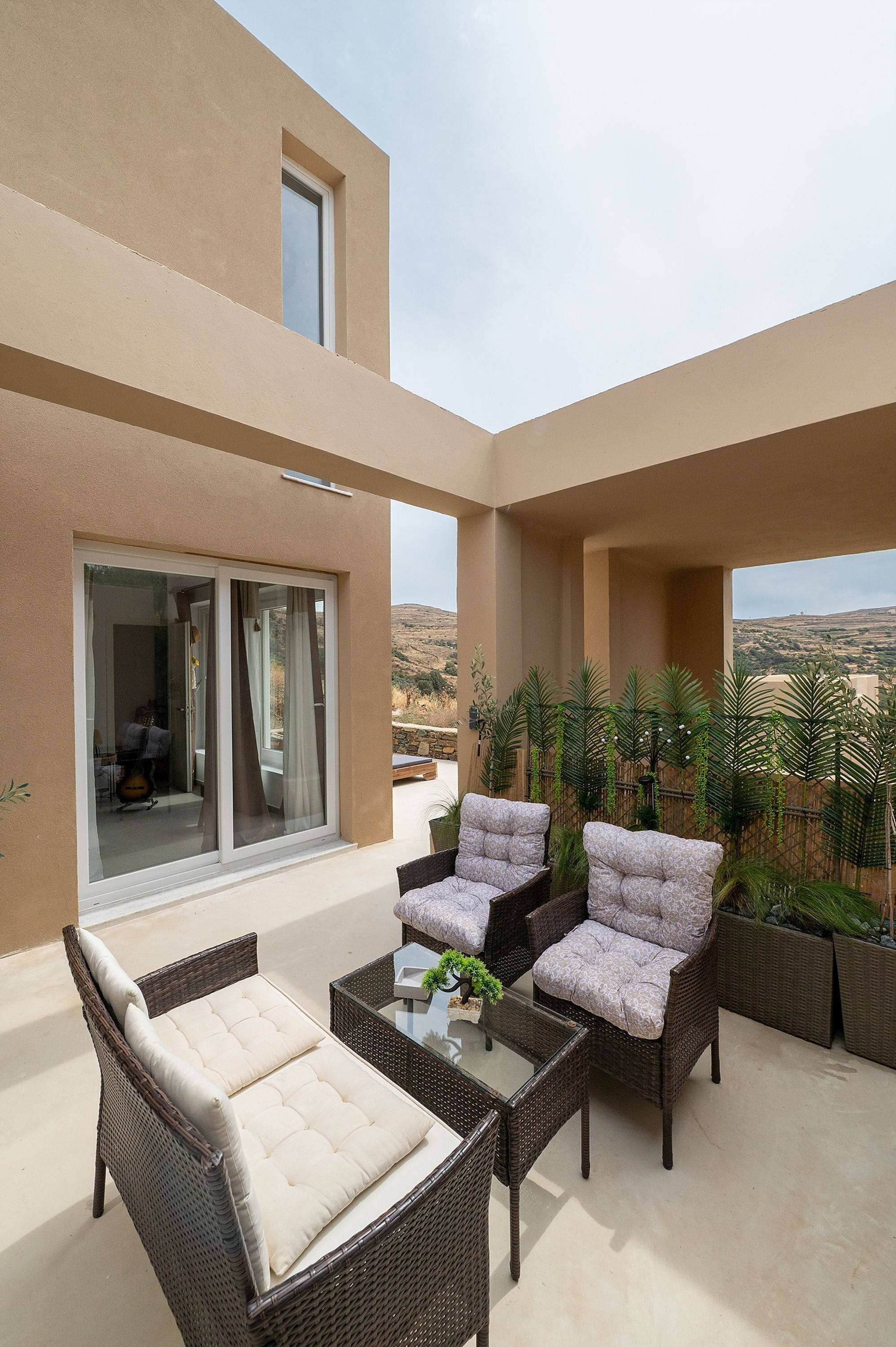 Ein Balkon mit Korbmöbeln, einem Glastisch und Blick auf die Landschaft.