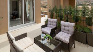 Uma varanda com móveis de vime, uma mesa de vidro e vista para a paisagem.