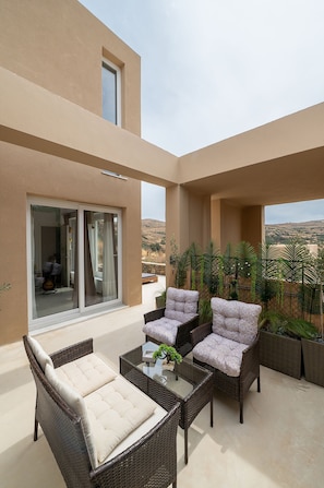 Ein Balkon mit Korbmöbeln, einem Glastisch und Blick auf die Landschaft.