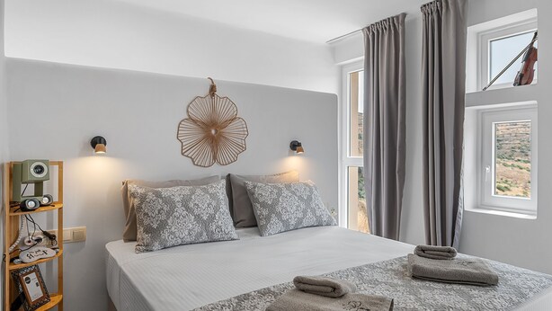 Quarto com cama, almofadas, um objeto decorativo na parede, abajures, janela com cortinas e vista para o exterior.