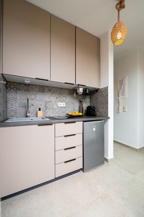 A modern kitchen with a built-in dishwasher, a coffee machine, and a hanging light fixture. - The Aer Element Of Gaea (Tinos)