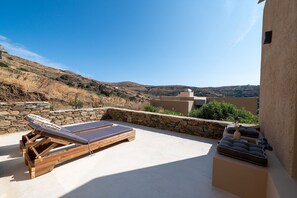 A rooftop terrace with lounge chairs and a stone wall, overlooking a hilly landscape. - The Aer Element Of Gaea (Tinos)