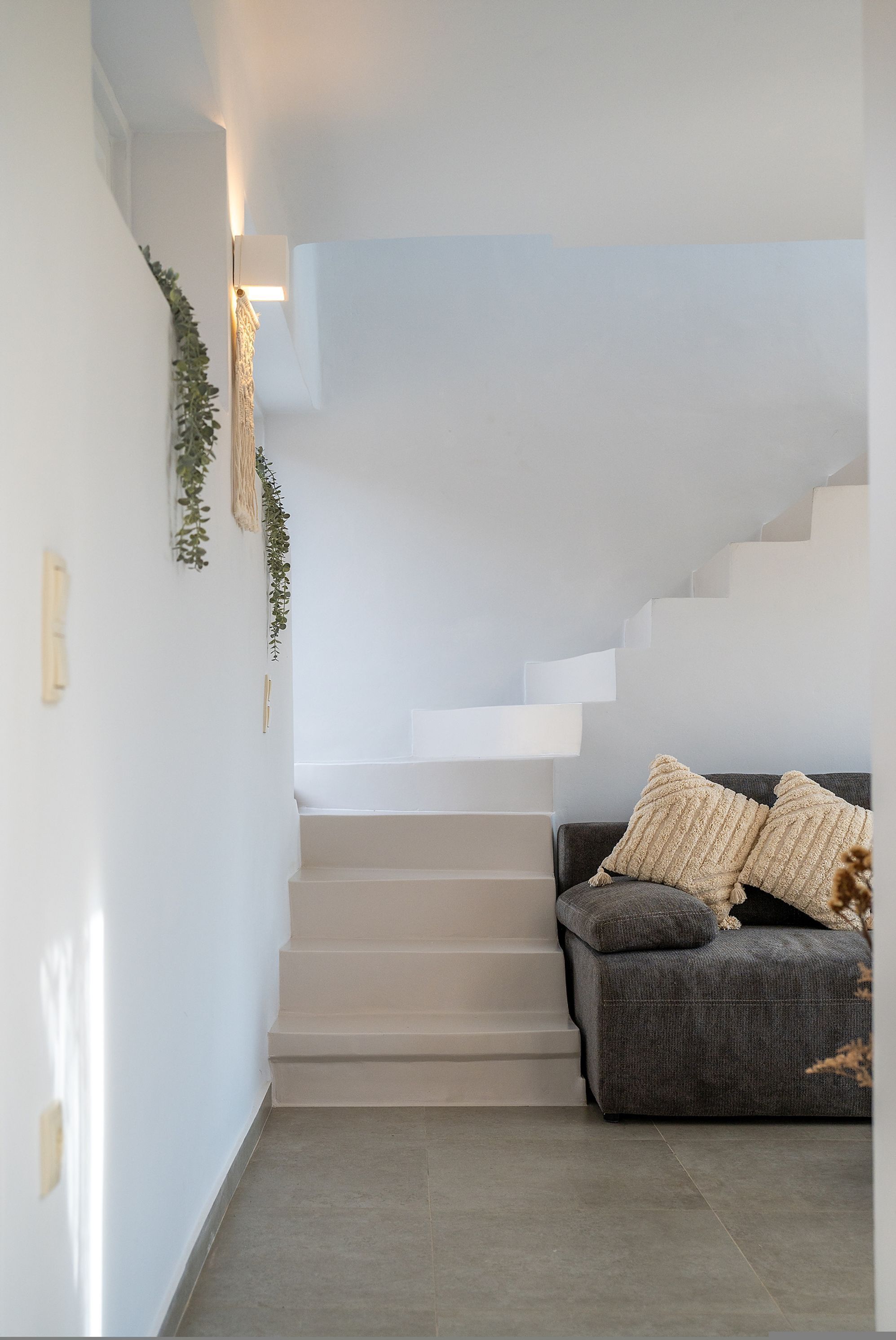 A staircase leading to an upper level, a grey sofa with cushions, and a wall-mounted light fixture.