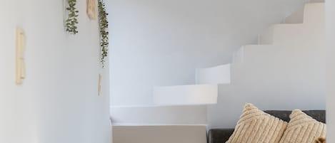 Una escalera que sube a un nivel superior, un sofá gris con cojines, y una lámpara fijada a la pared.