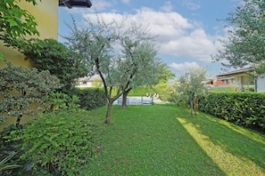 A well-maintained garden with a variety of trees and shrubs, a clear sky, and a fence in the background. - Raffa Holiday in Raffa (Puegnago del Garda)