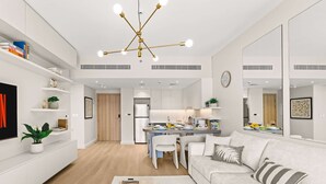A modern living room with a sofa, coffee table, and a dining area with chairs and a table. - Stayshort Stylish 1BR Apartment Near Burj Al Arab Family-friendly Sleeps 4 (Dubai)