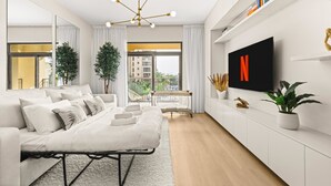 A modern living room with a sofa, a coffee table, a TV mounted on the wall, and a large window. - Stayshort Stylish 1BR Apartment Near Burj Al Arab Family-friendly Sleeps 4 (Dubai)