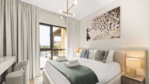 A modern hotel room with a large bed, a desk, a chair, a nightstand, and a painting on the wall. - Stayshort Stylish 1BR Apartment Near Burj Al Arab Family-friendly Sleeps 4 (Dubai)