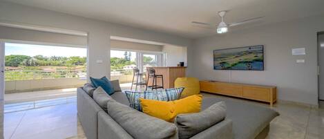 A modern living room with a grey sofa, yellow cushions, a wooden bench, and a painting on the wall.