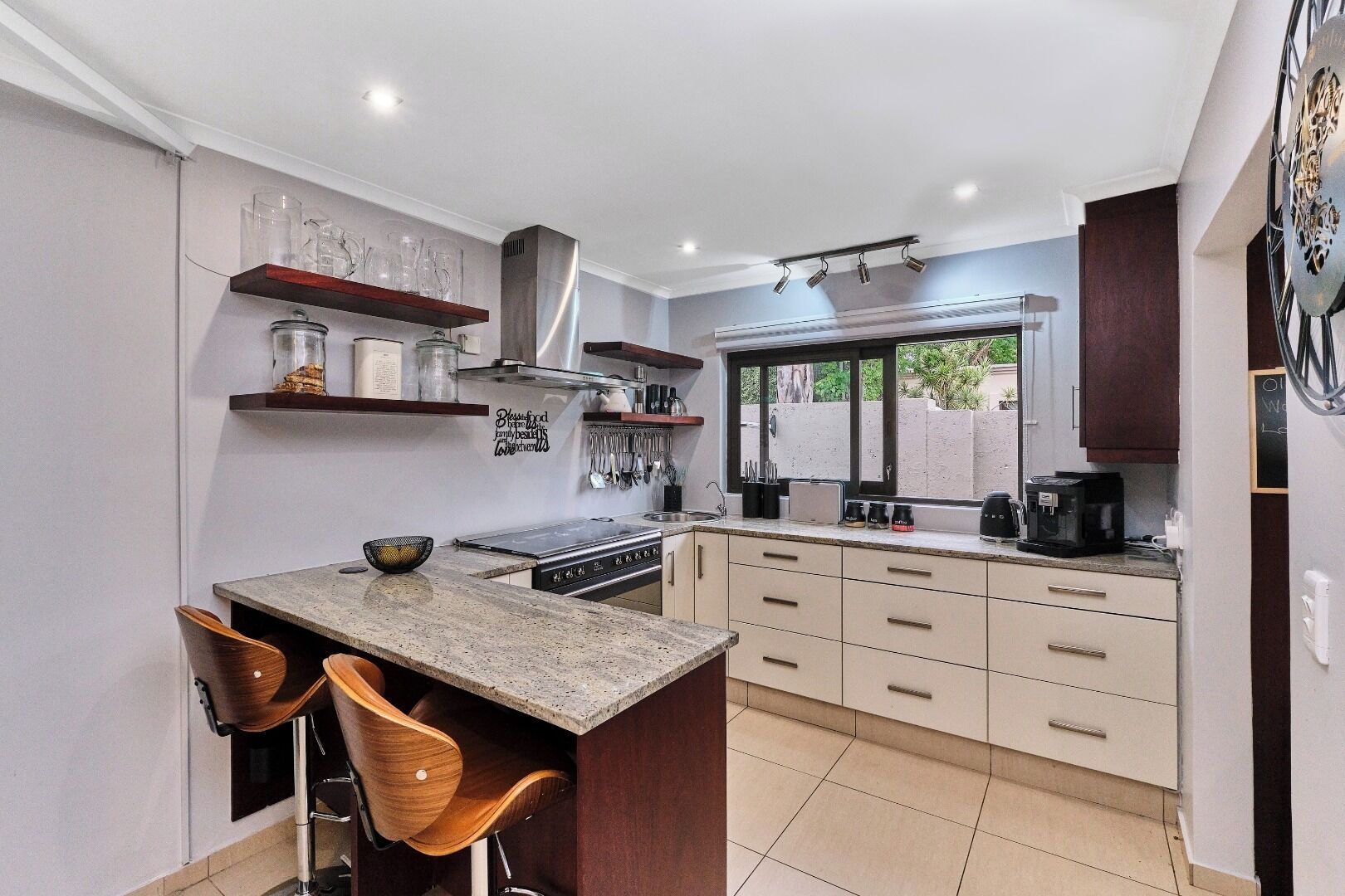 A modern kitchen with a central island, bar stools, a built-in oven, and a window providing a view of the outdoors.
