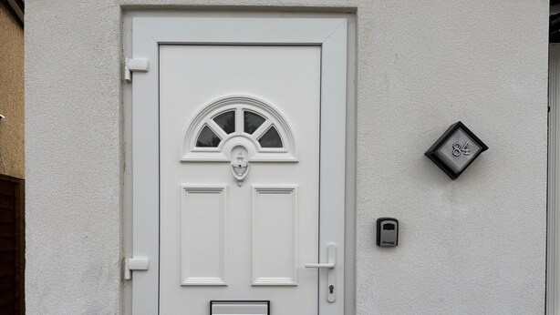 Una puerta blanca con un buzón, un letrero con el número de la casa y una cámara de seguridad encima.