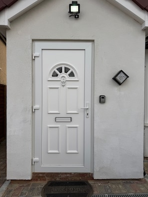 Una puerta blanca con un buzón, un letrero con el número de la casa y una cámara de seguridad encima.