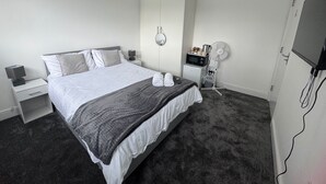 Una habitación de hotel con cama, mesitas de noche, televisor, microondas y ventilador.