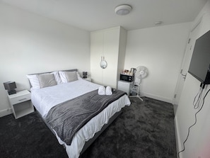 Una habitación de hotel con cama, mesitas de noche, televisor, microondas y ventilador.