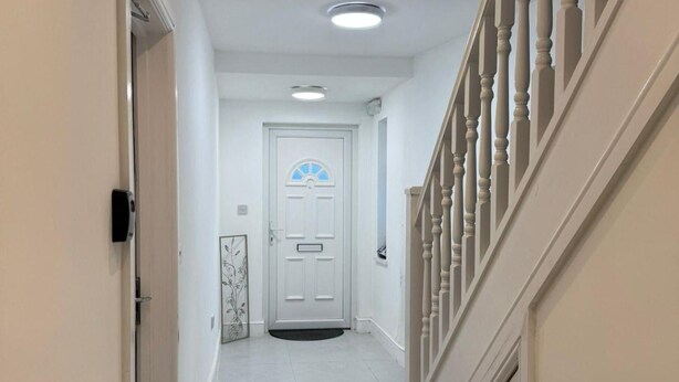 Un pasillo con una puerta blanca, un panel de vidrio decorativo y una escalera con barandilla.