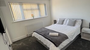 Un dormitorio con una cama grande, una ventana con persianas, una mesita de noche con lámpara y un radiador.