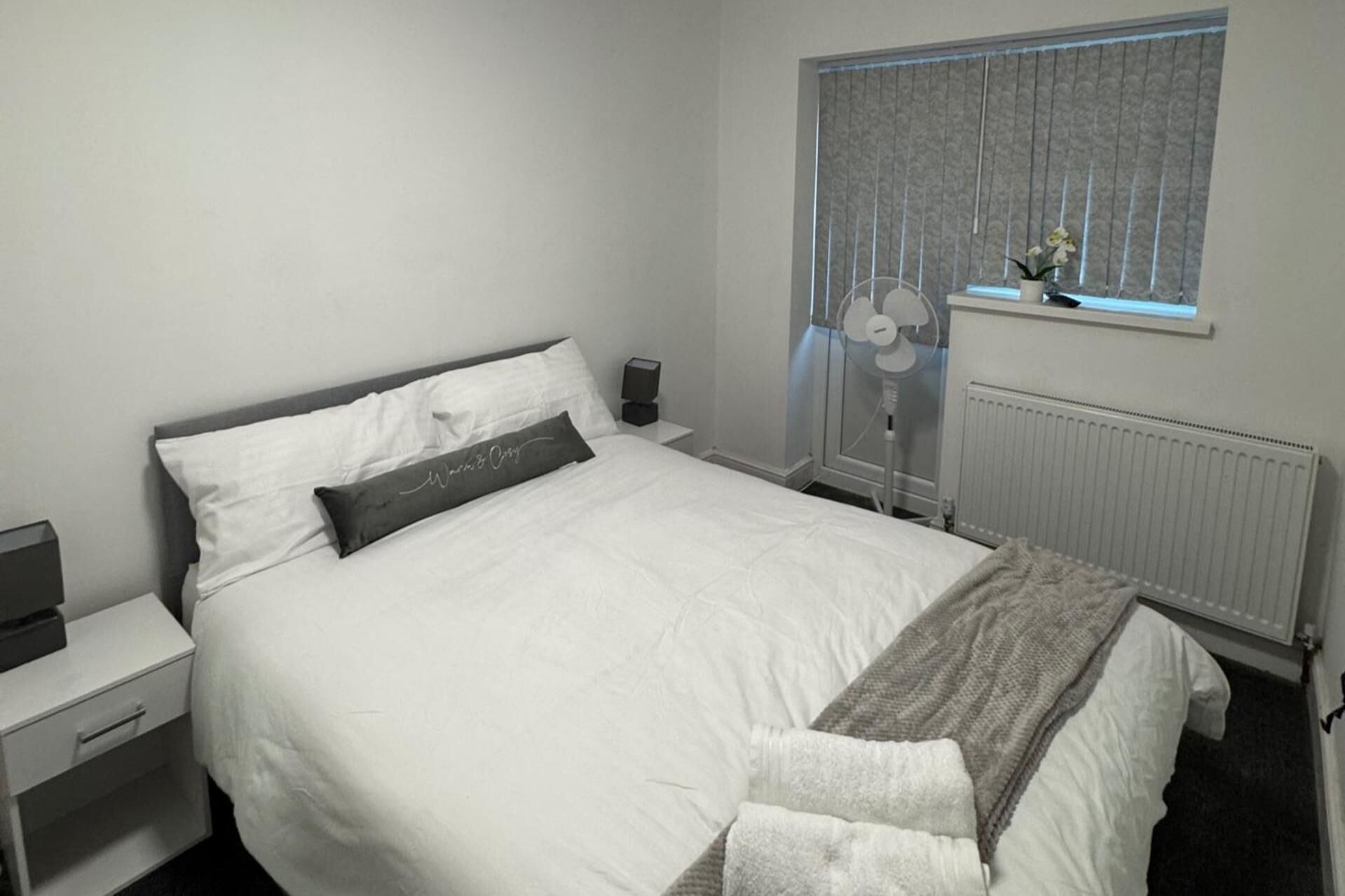 A neatly made bed with a pillow, a bedside table with a lamp, and a window with curtains.