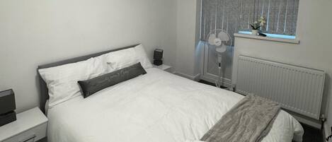 A neatly made bed with a pillow, a bedside table with a lamp, and a window with curtains.
