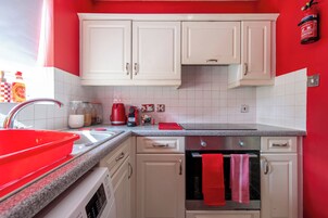 Una cocina con armarios blancos, un lavabo rojo y una tetera roja.