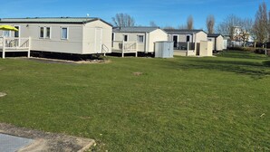 A row of mobile homes with a grassy yard and a clear blue sky. - 8 Berth Caravan at Butlins Skegness (Skegness)