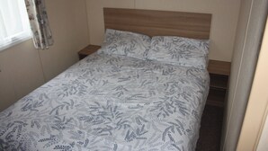 A single bed with a patterned bedspread in a room with a wooden headboard and a window with curtains. - 6 Berth Caravan Butlins Skegness Pet Friendly (Skegness)