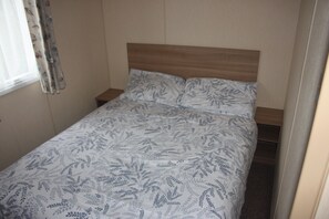 A single bed with a patterned bedspread in a room with a wooden headboard and a window with curtains. - 6 Berth Caravan Butlins Skegness Pet Friendly (Skegness)
