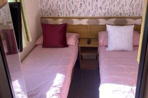A compact bedroom with two beds, each with a pillow and a bedside table. - 8 Berth Caravan at Butlins Skegness (Skegness)