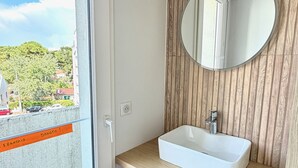 A bathroom with a white sink, a round mirror, and a wooden panel wall. - Face mer à La Baule : Evobaule (La Baule-Escoublac)