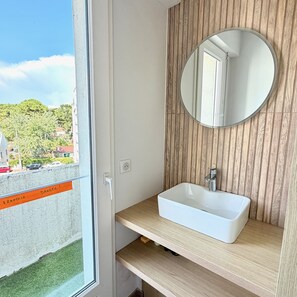 Ein Badezimmer mit einem weißen Waschbecken, einem runden Spiegel und einer Wand aus Holzpaneelen.
