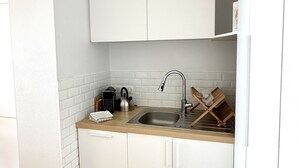 A compact kitchen with white cabinetry, a stainless steel sink, and a kettle. - Face mer à La Baule : Evobaule (La Baule-Escoublac)