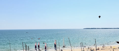 Una playa con veleros, cielo despejado y una costa lejana.