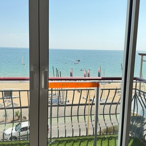 Blick auf das Meer vom Balkon, mit Sicherheitshinweis, einem Sandstrand und geparkten Autos.