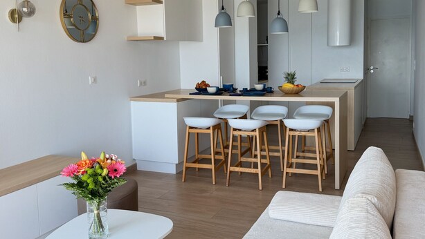 A modern kitchen with a central island, wooden stools, pendant lighting, and a white dining table. - Face mer à La Baule : Evobaule (La Baule-Escoublac)
