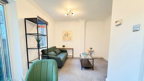 A living room with a green sofa, a glass coffee table, a bookshelf, and a small table with a plant. - Prime City of London Accommodation (London)