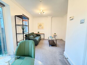 A living room with a green sofa, a glass coffee table, a bookshelf, and a small table with a plant. - Prime City of London Accommodation (London)