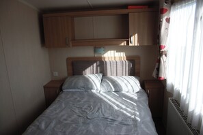 A single bed with a headboard, two bedside tables, and a window with curtains. - 8 Berth Caravan at Butlins Skegness Pet Friendly (Skegness)