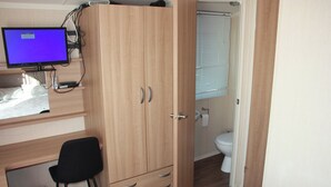 Een slaapkamer met een houten garderobe, een bureau met een computermonitor, een zwarte stoel en een badkamer met toilet en wastafel.