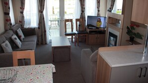 Een gezellige, compacte leefruimte met een bank, een eettafel, een televisie en een kitchenette.