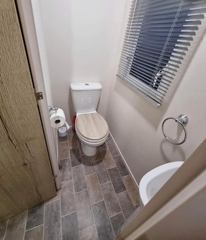 Ein kleines Badezimmer mit Toilette, Bidet, Toilettenpapierhalter und einem Fenster mit Jalousien.
