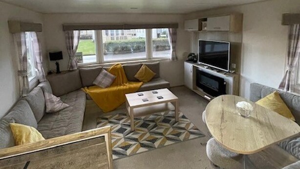 A compact living space with a sofa, a coffee table, a TV, and a dining area. - 8 Berth Caravan Butlins Skegness (Skegness)