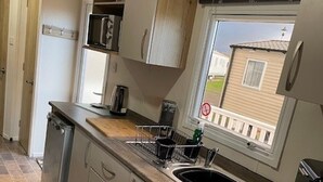 A compact kitchen with a built-in oven, a sink, and a window overlooking a residential area. - 8 Berth Caravan Butlins Skegness (Skegness)