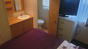 Ein Schlafzimmer mit einem Bett, einem Nachttisch mit Fernseher, einem Badezimmer mit Toilette und Waschbecken sowie Holzschränken.