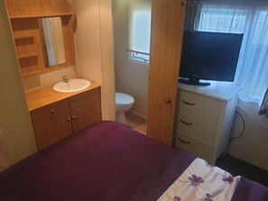 Ein Schlafzimmer mit einem Bett, einem Nachttisch mit Fernseher, einem Badezimmer mit Toilette und Waschbecken sowie Holzschränken.