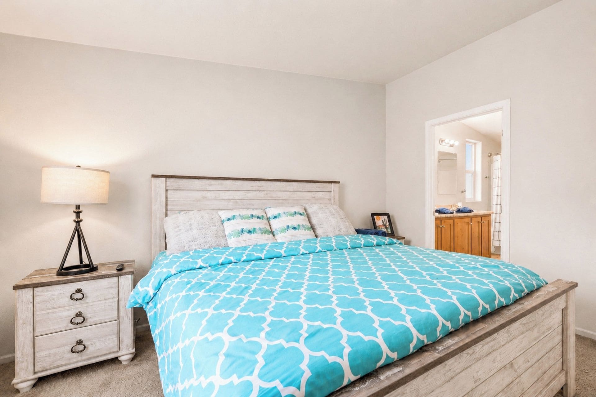 A bedroom with a bed, bedside table, lamp, and a view of the bathroom.
