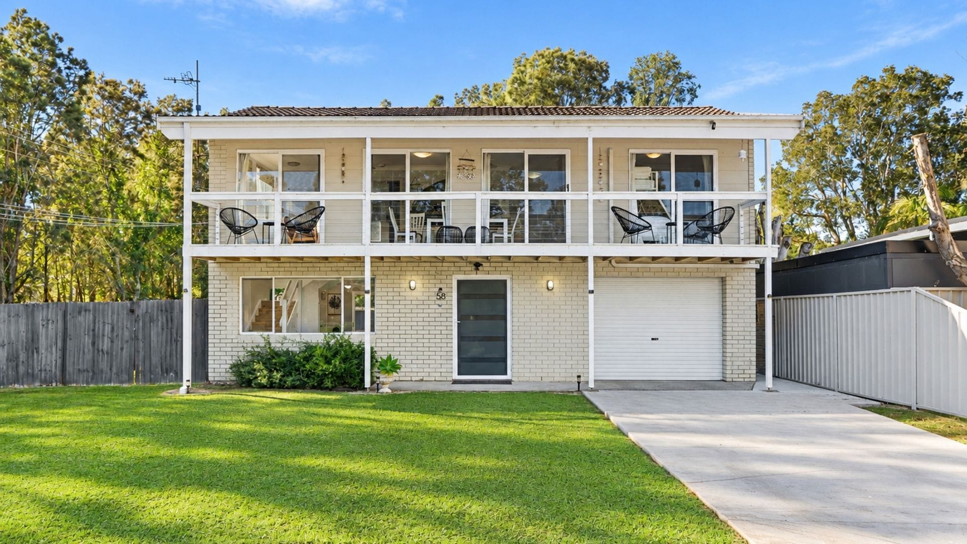 A two-story residential building with a front garage, a covered porch with outdoor seating, and a well-maintained lawn.