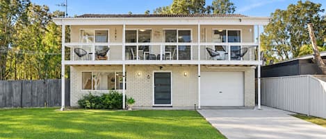 A two-story residential building with a front garage, a covered porch with outdoor seating, and a well-maintained lawn.